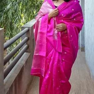 Woman wearing a bright pink handloom silk Chanderi saree with intricate designs, standing on a balcony.