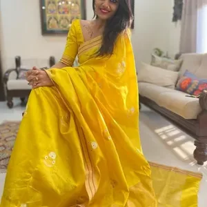 A woman wearing a bright yellow Handloom Pure Silk Chanderi Saree with subtle white embroidery/motifs and a thin gold border, seated indoors on a chair/sofa.